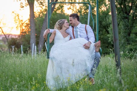 A bride and groom sitting on the ground in a swing.
