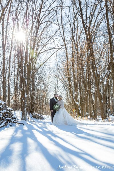 A bride and groom pose for a picture in the snow.
