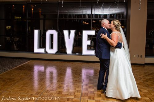 A bride and groom kissing in front of the word love.