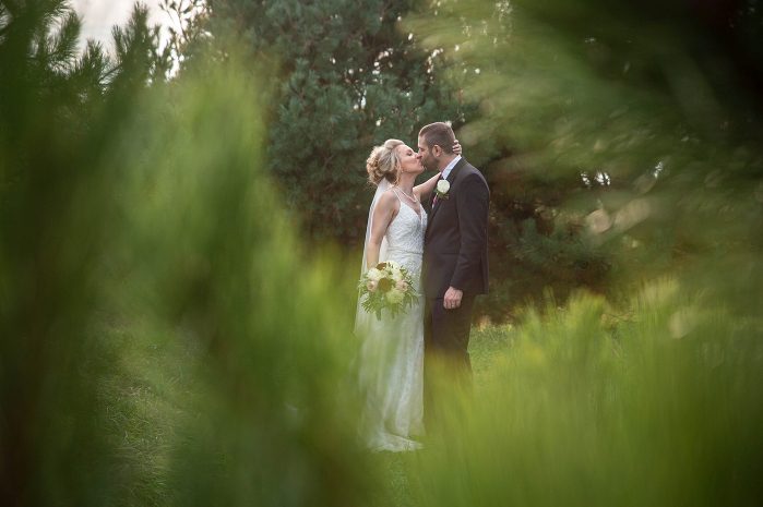 A bride and groom kissing in the middle of a field.