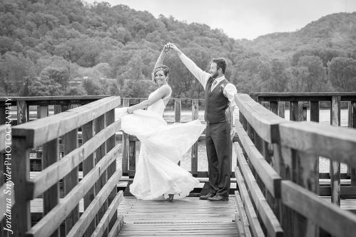 A bride and groom are holding hands on the bridge.