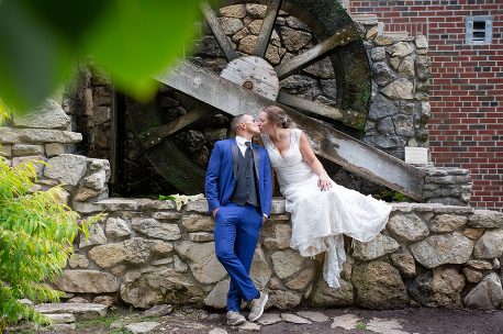 A man and woman kissing in front of a water wheel.