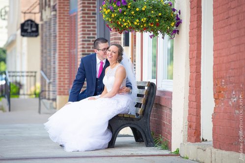 A bride and groom sitting on the bench outside