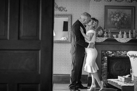 A man and woman kissing in front of a fireplace.