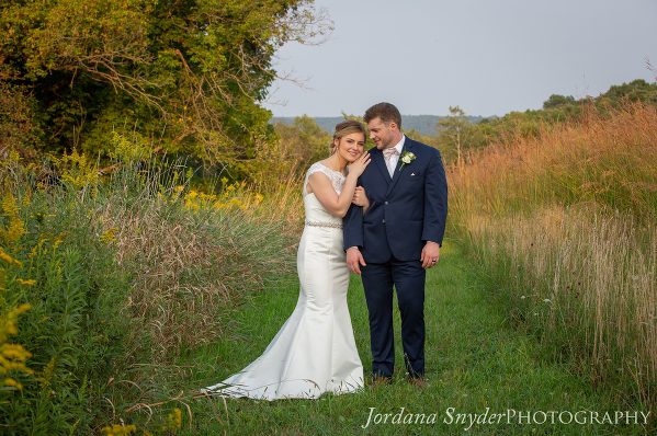 A bride and groom pose for a picture in the grass.