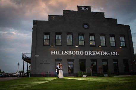A bride and groom standing in front of the hillsboro brewing company.