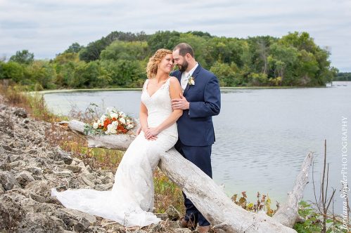 A bride and groom pose for a picture by the water.