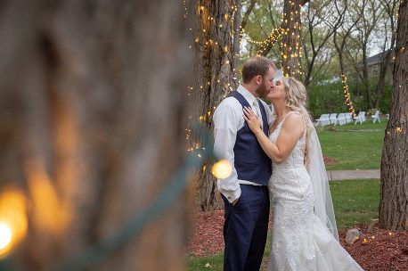 A bride and groom kissing in front of trees.