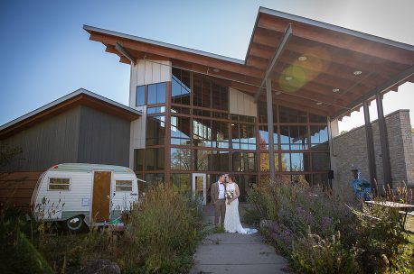 A bride and groom are standing outside of their wedding venue.