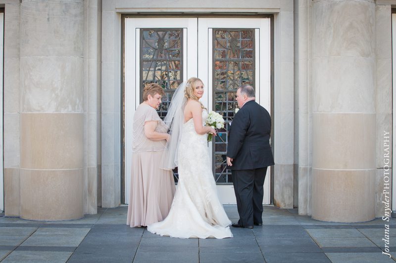 A bride and her parents standing outside of the church.