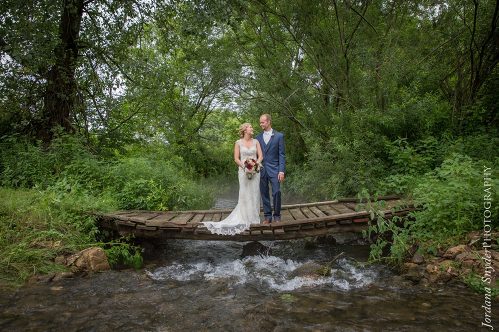 A bride and groom standing on a bridge over water.