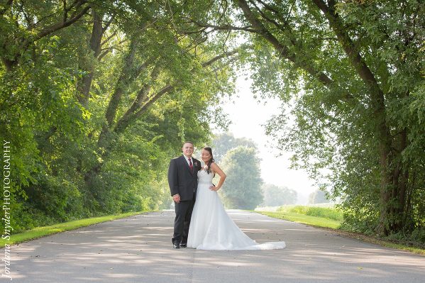 A bride and groom pose for a picture on the side of a road.