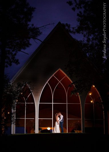 A bride and groom standing in front of a church at night.