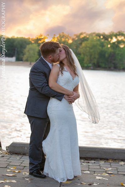 A bride and groom kissing in front of the water.