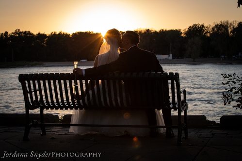 A couple sitting on top of a bench at sunset.