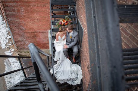 A bride and groom sitting on stairs in front of a brick wall.