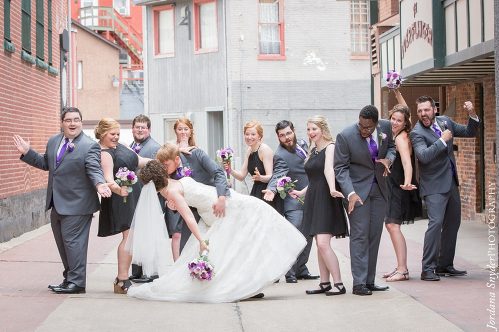 A bride and groom kissing in front of their wedding party.