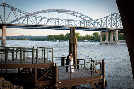 A bride and groom standing on the dock of a pier.