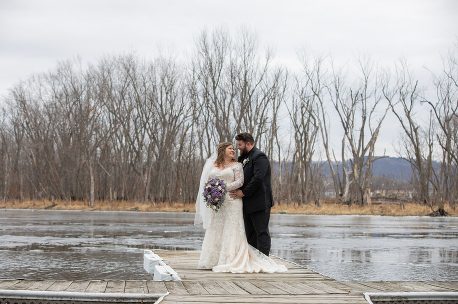 A bride and groom standing on the edge of a pier.