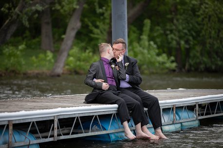 Two men sitting on a dock next to water.