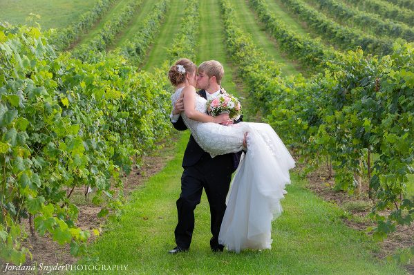 A bride and groom kissing in the middle of a vineyard.