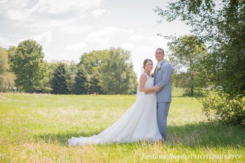 A bride and groom pose for a picture in the grass.