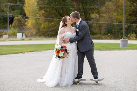 A bride and groom kissing on the side of a skateboard.