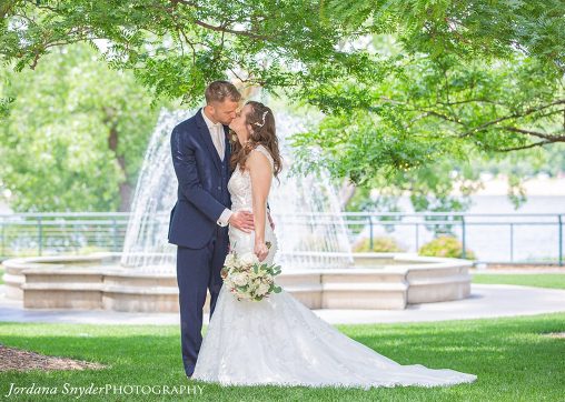 A bride and groom kissing in front of a fountain.