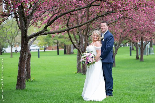 A bride and groom pose for a picture in the park.