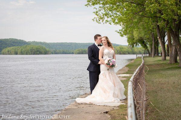 A bride and groom standing next to the water.
