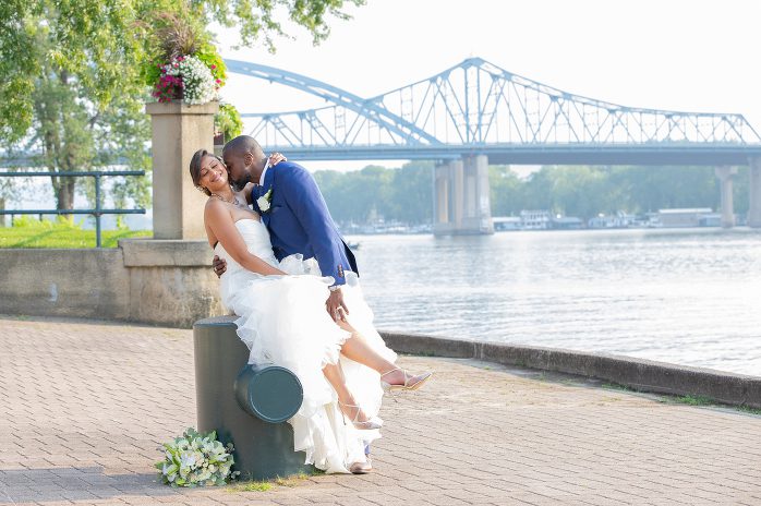 A bride and groom kissing on the side of a water way.
