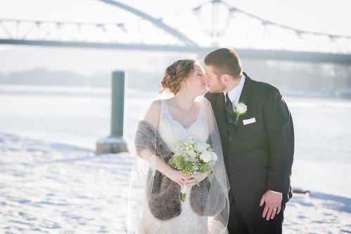 A bride and groom kissing in front of the water.