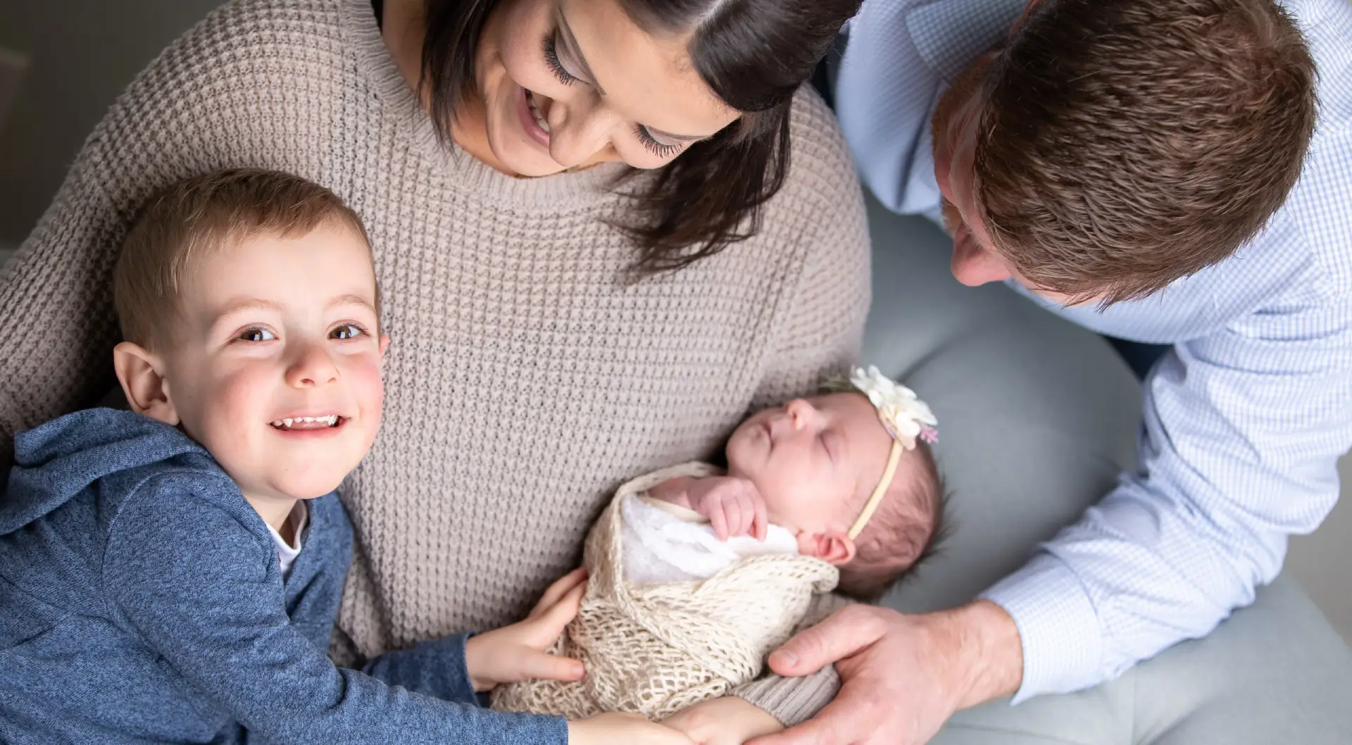 A woman holding a baby while two children watch.