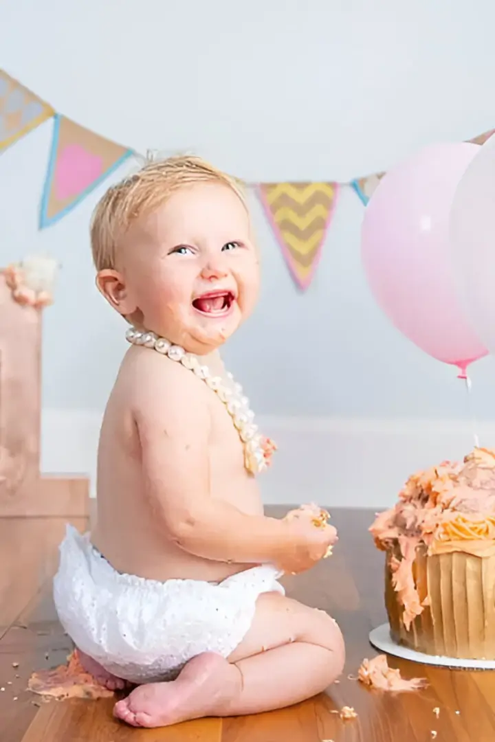 A baby in diapers with pearls and a cake.