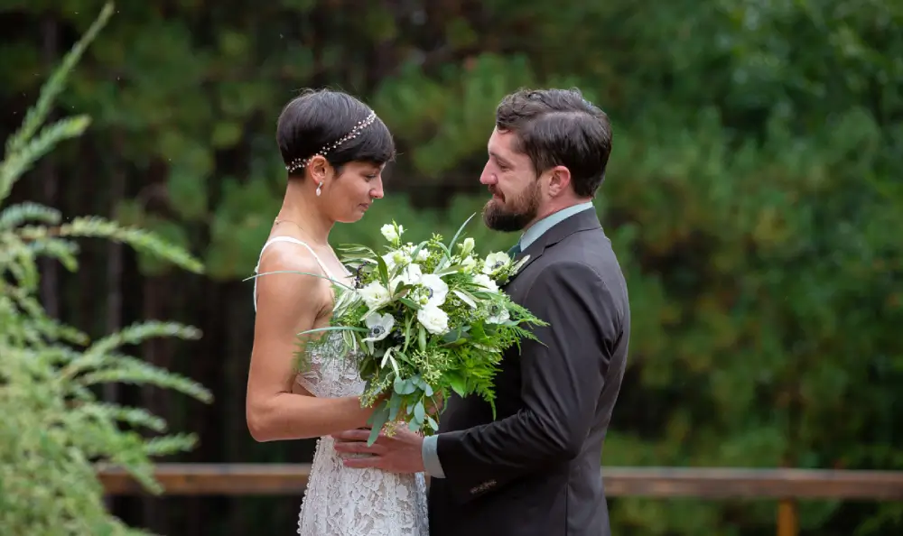 A man and woman holding flowers in front of trees.