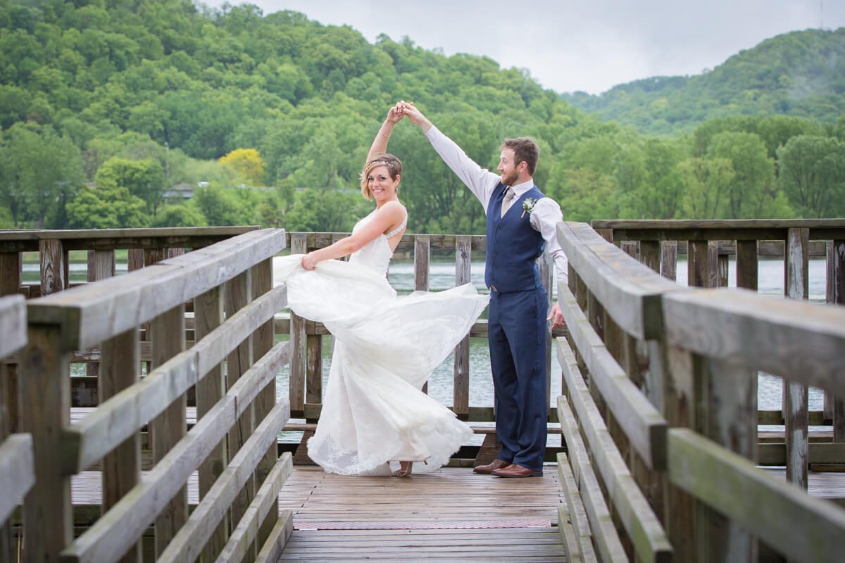 A bride and groom pose for the camera on a bridge.