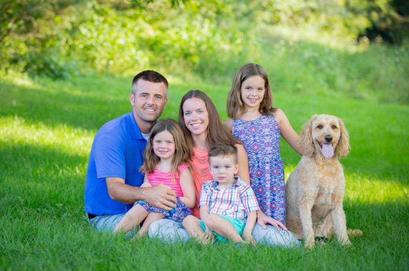 A family sitting in the grass with their dog.