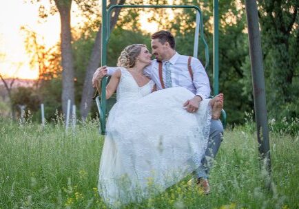 A bride and groom sitting on the ground in a swing.
