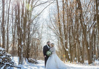A bride and groom pose for a picture in the snow.
