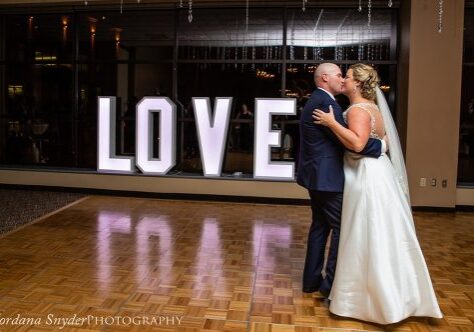 A bride and groom kissing in front of the word love.