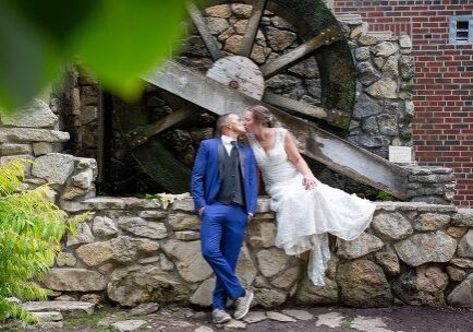 A man and woman kissing in front of a water wheel.