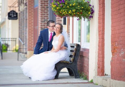 A bride and groom sitting on the bench outside