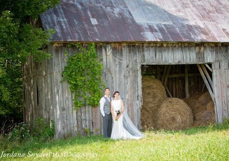 A bride and groom standing in front of an old barn.