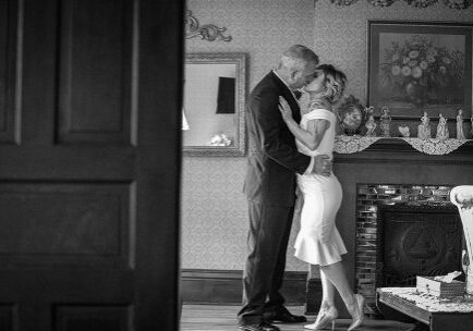 A man and woman kissing in front of a fireplace.