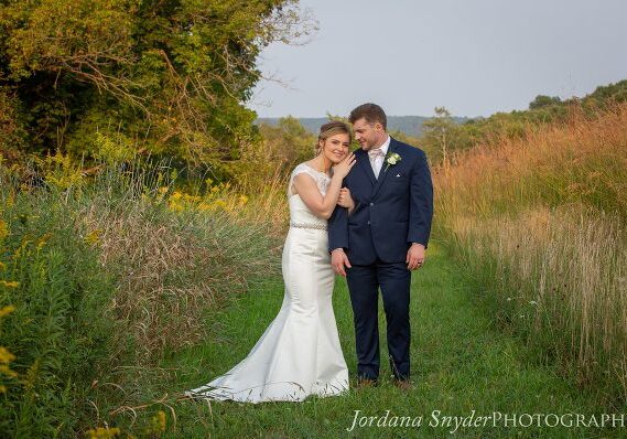 A bride and groom pose for a picture in the grass.