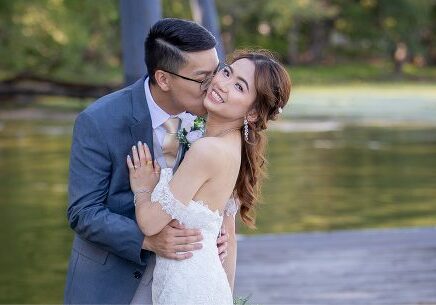 A man and woman kissing in front of a body of water.