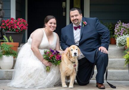 A bride and groom pose with their dog.