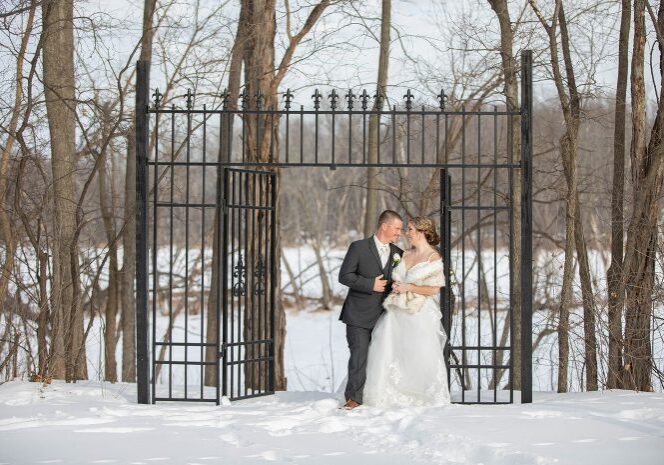 A man and woman kissing in front of a black iron gate.