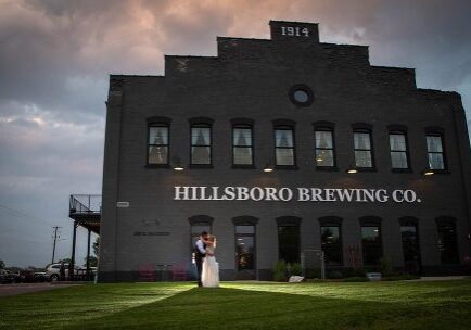 A bride and groom standing in front of the hillsboro brewing company.