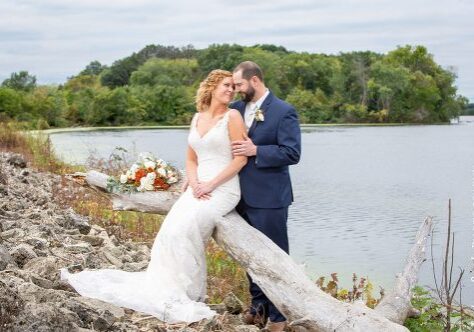 A bride and groom pose for a picture by the water.